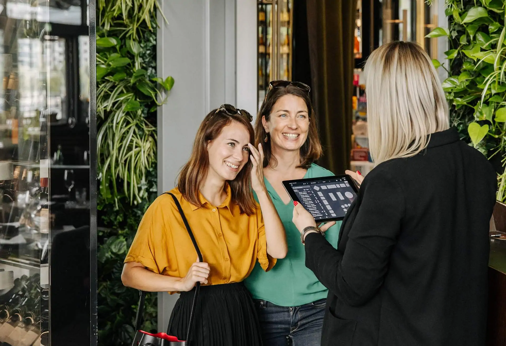 Two guests checking in with their restaurant reservation while the server is assigning their table looking at a tablet