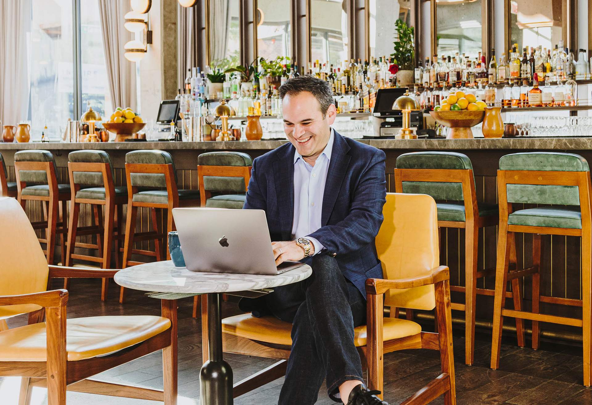 Image depicts a restaurant owner working on a laptop. The man is sitting at one of the restaurant tables