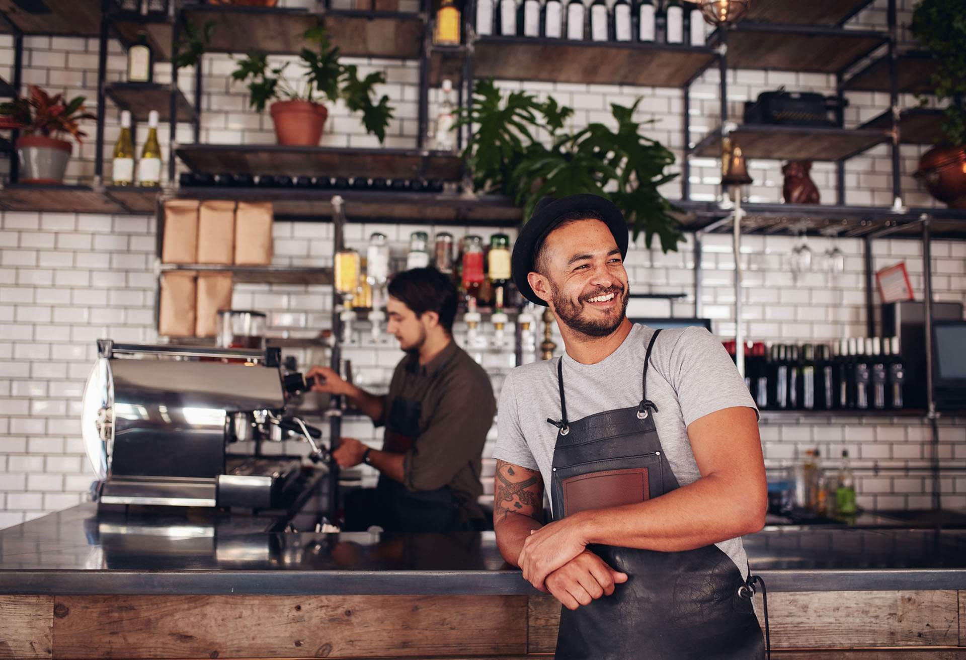 A waiter leaning on the bar counter and smiling. They wear an apron and a tshirt