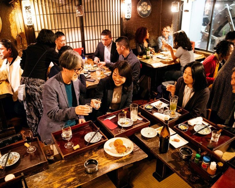 Diners eating and cheering at an Asian restaurant, with food, plates and drinks on a bar table