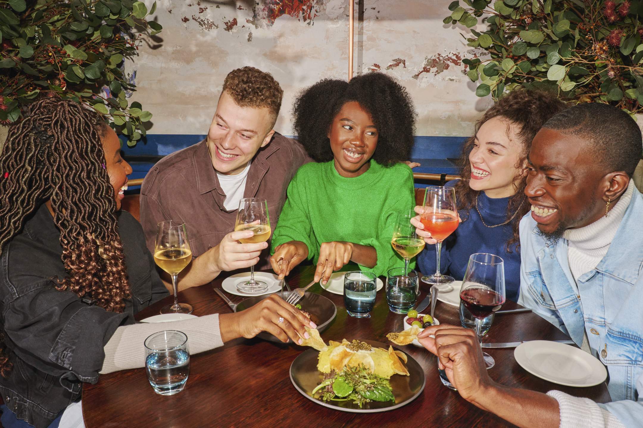 The image shows a group of customers sitting at a restaurant. The group is mixed in terms of gender and ethnicity, they are laughing and enjoying their meal.